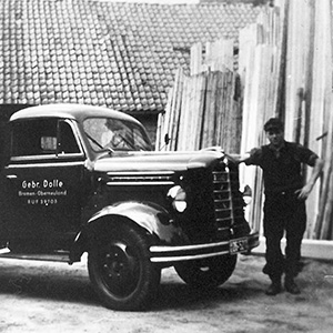 Foto in bianco e nero del primo dipendente Dolle accanto a un camion d’epoca carico di legname.