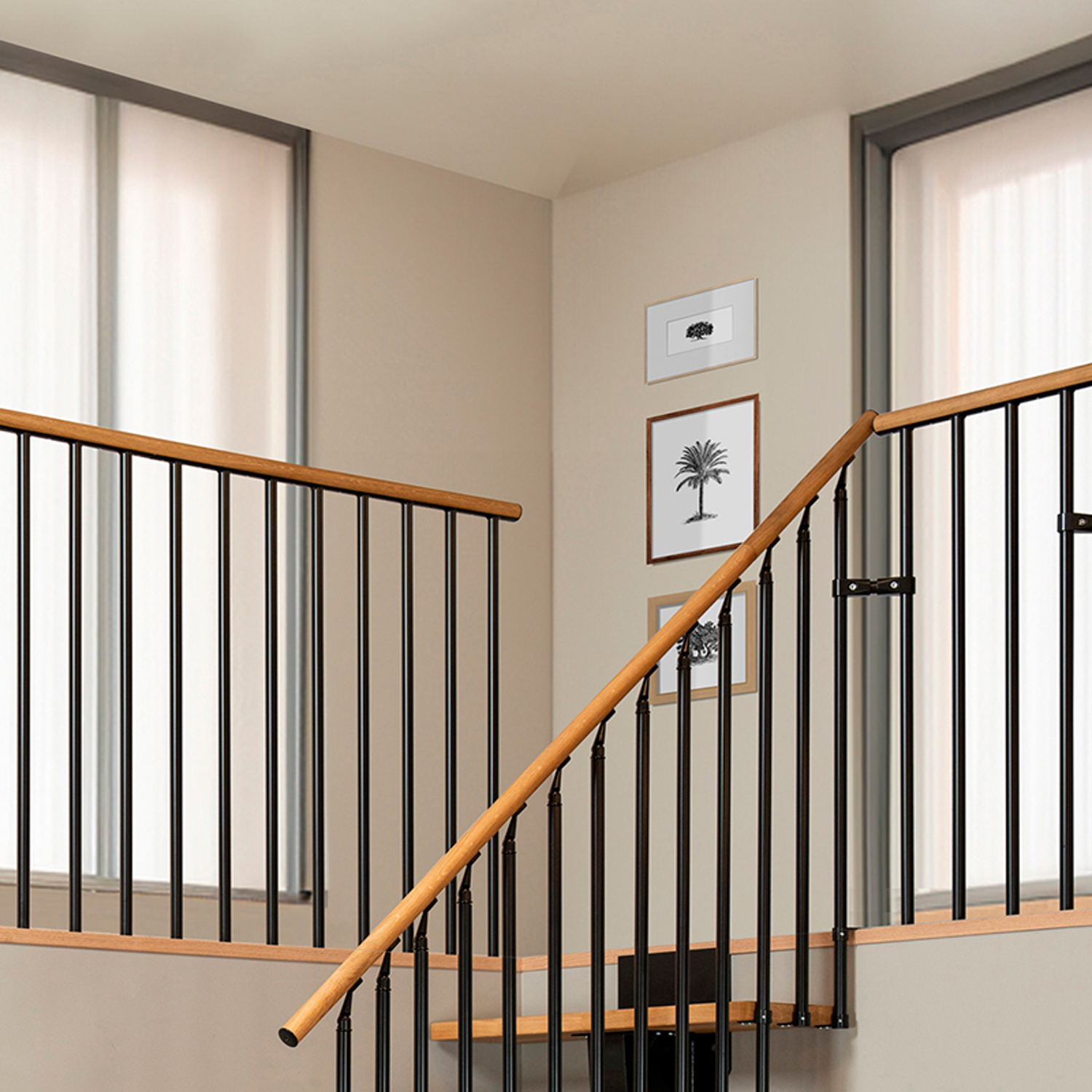Scala con corrimano in legno e balaustre verticali nere, su sfondo di pareti chiare con opere incorniciate.