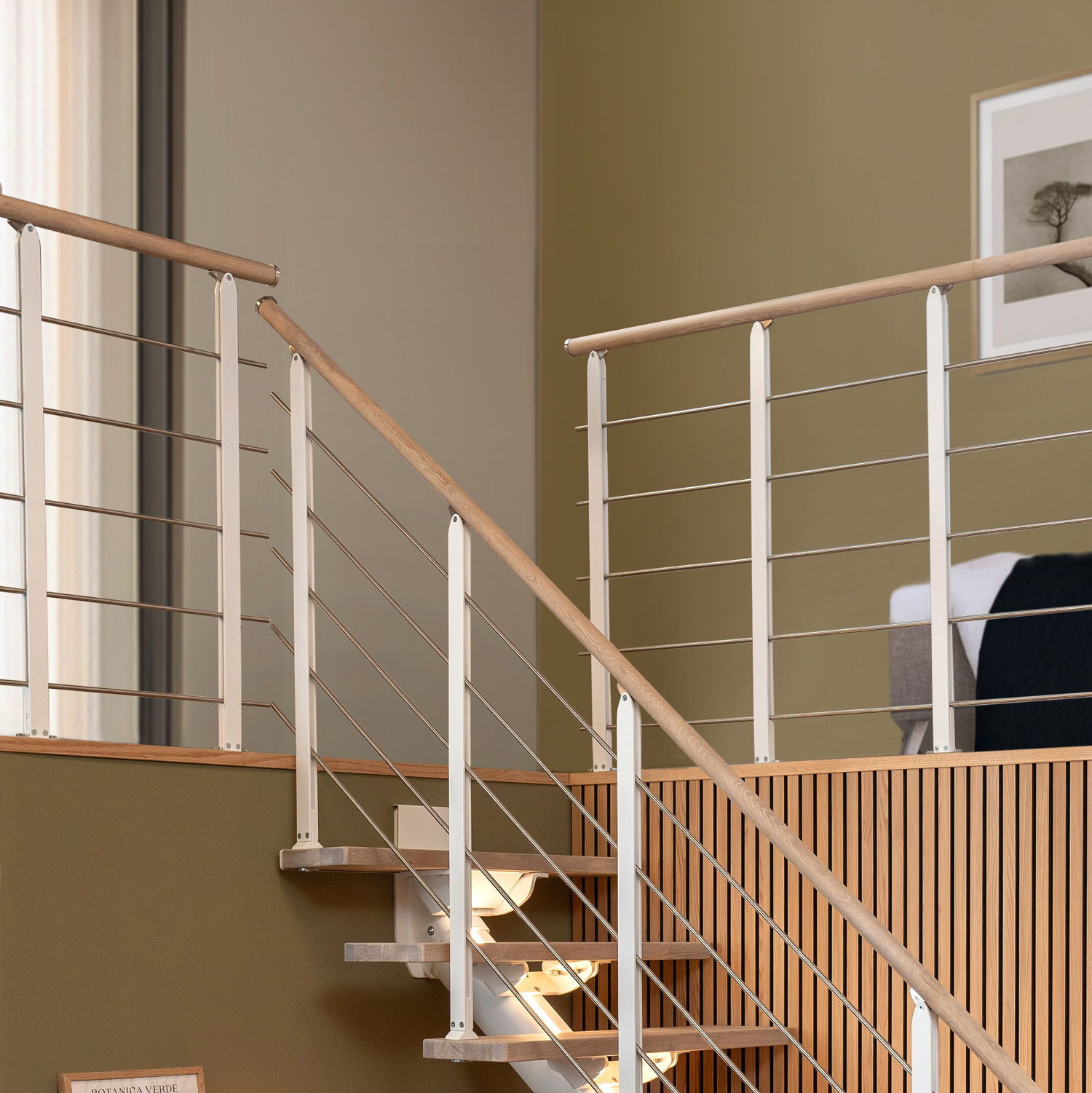 Scala moderna con ringhiera in legno chiaro e balaustre in metallo bianco, arricchita da cavi in acciaio orizzontali.