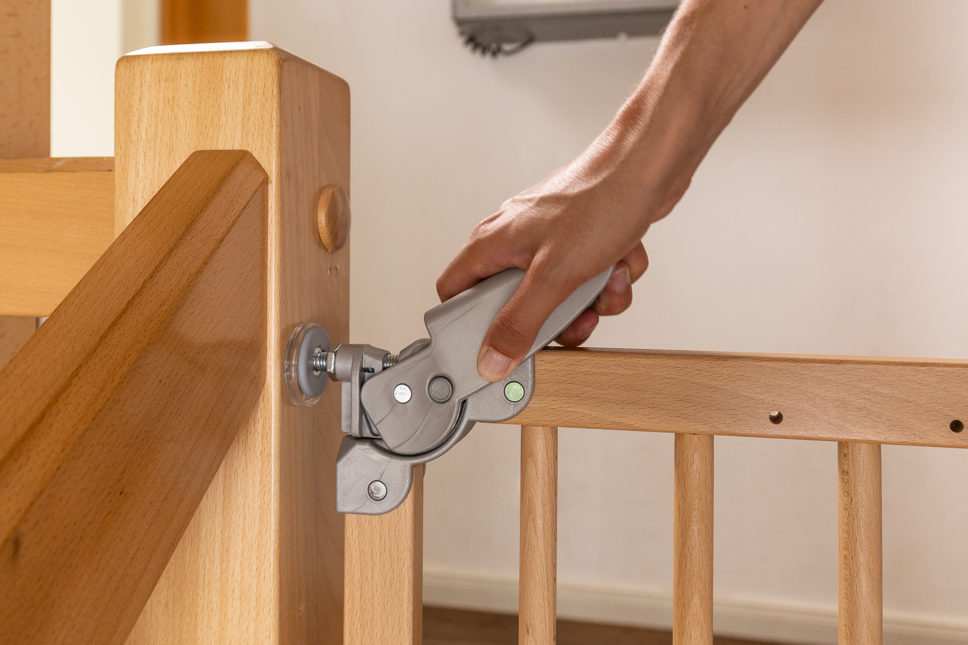 Mano che aziona la chiusura di sicurezza di un cancelletto di sicurezza in legno SOGEM, con un pratico sistema di apertura con una mano, saldamente fissato a un corrimano di scala.
