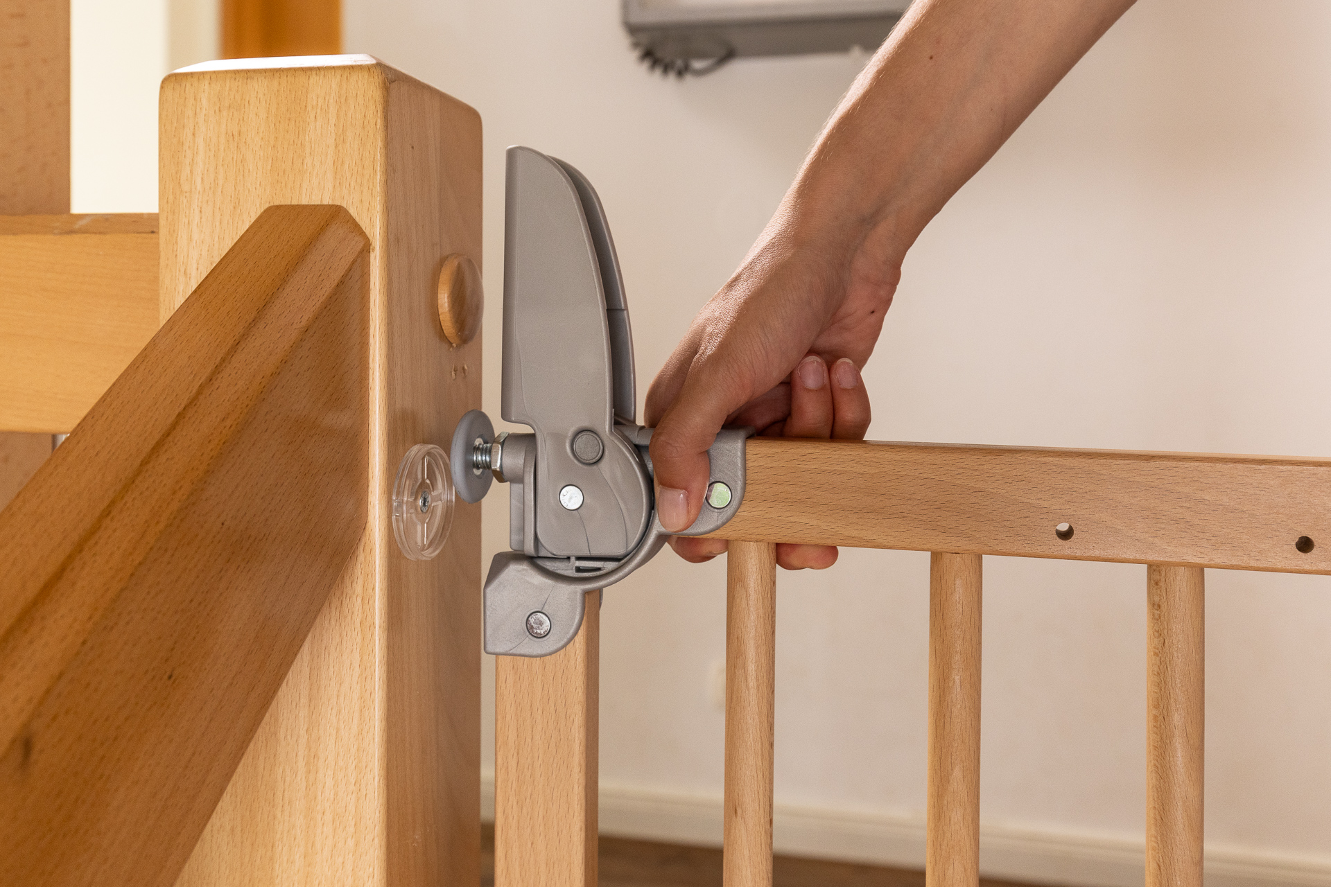 Mano che maneggia la chiusura di sicurezza chiusa di un cancelletto di sicurezza in legno SOGEM, illustrando il sistema di chiusura sicuro con una mano, fissato a un corrimano di scala.