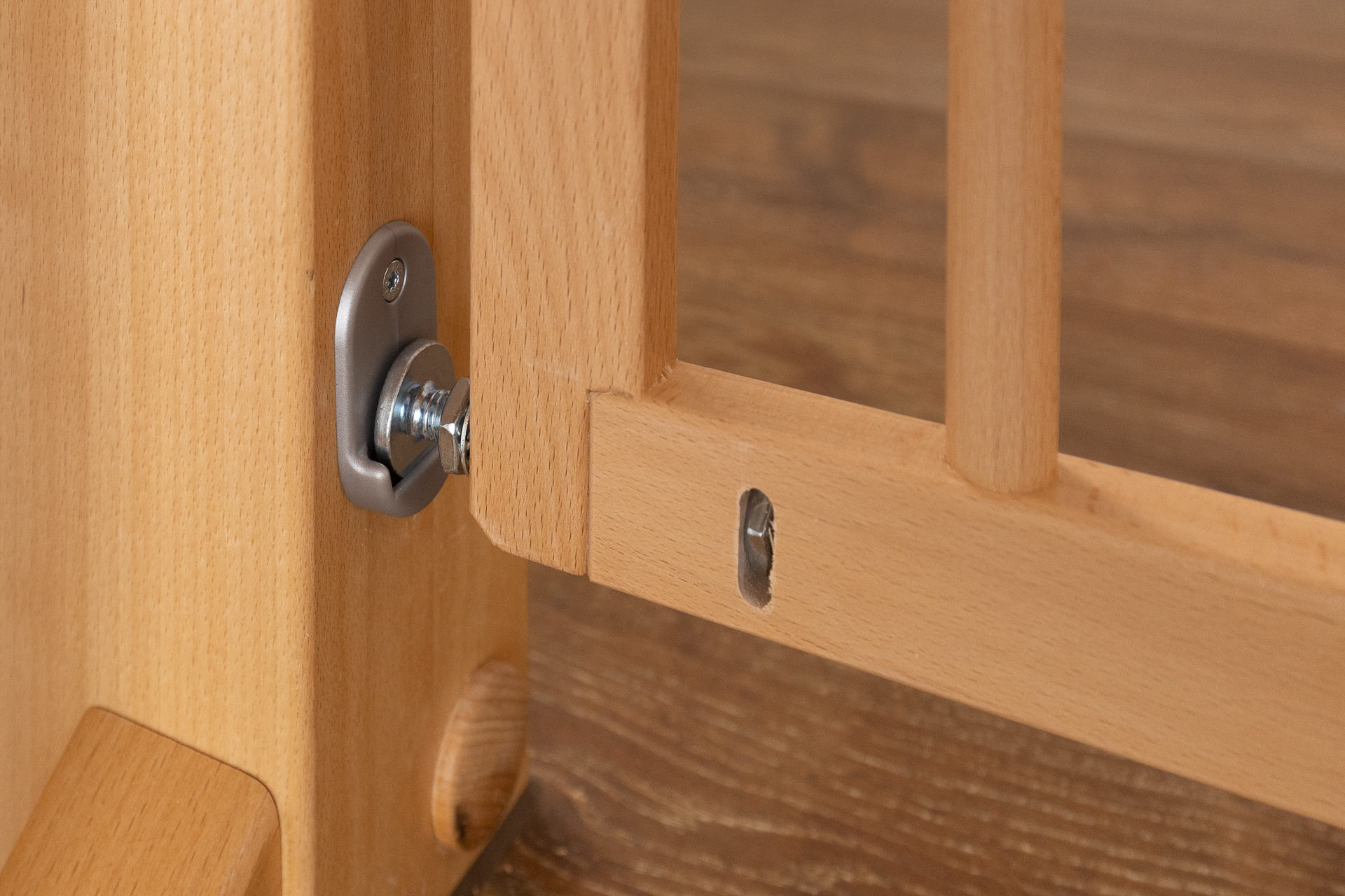 Primo piano del sistema di fissaggio avvitato di un cancelletto di sicurezza in legno, saldamente fissato a una parete con finitura metallica.